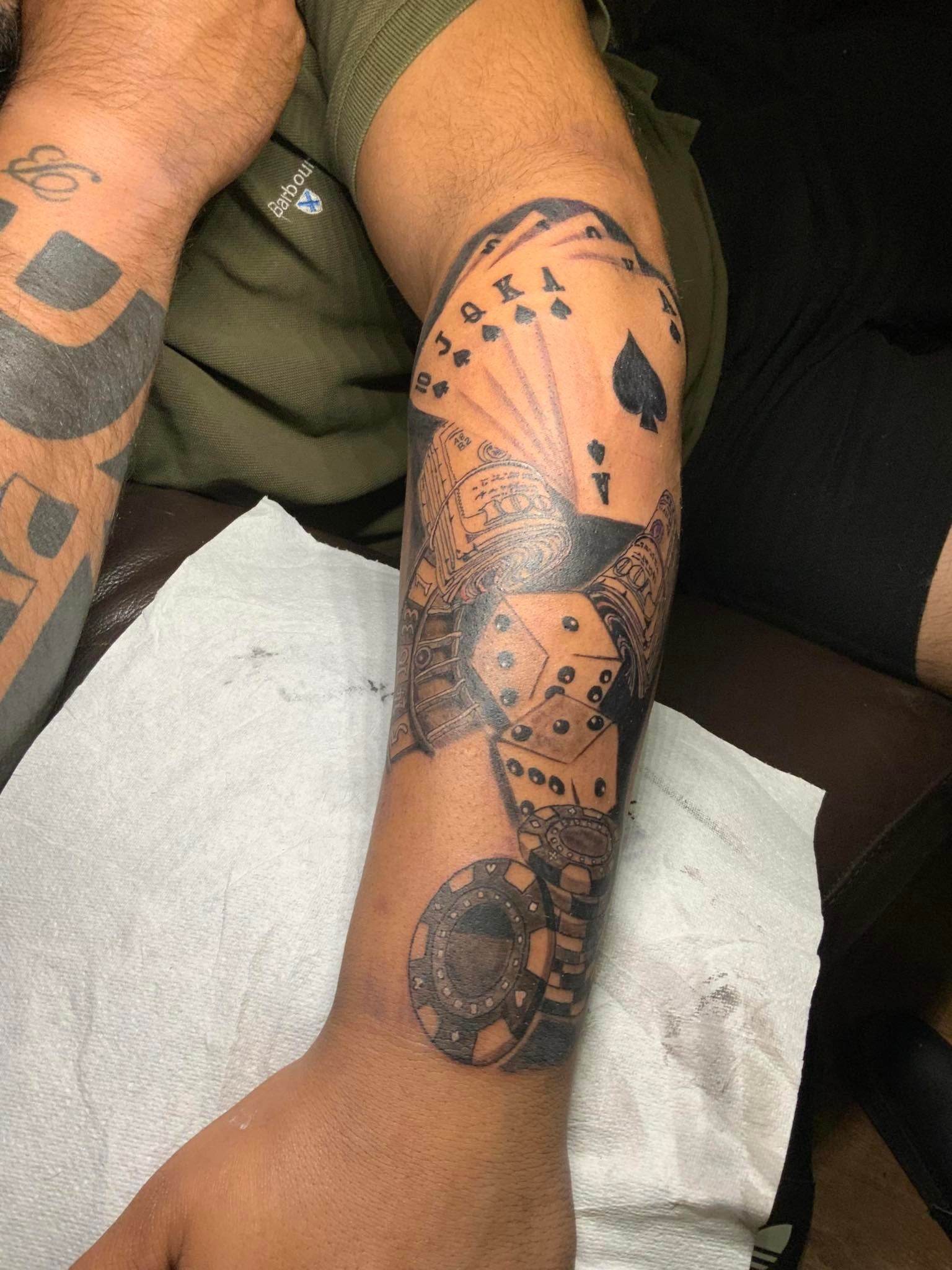 The forearm of a man covered in a tattoo about poker cards