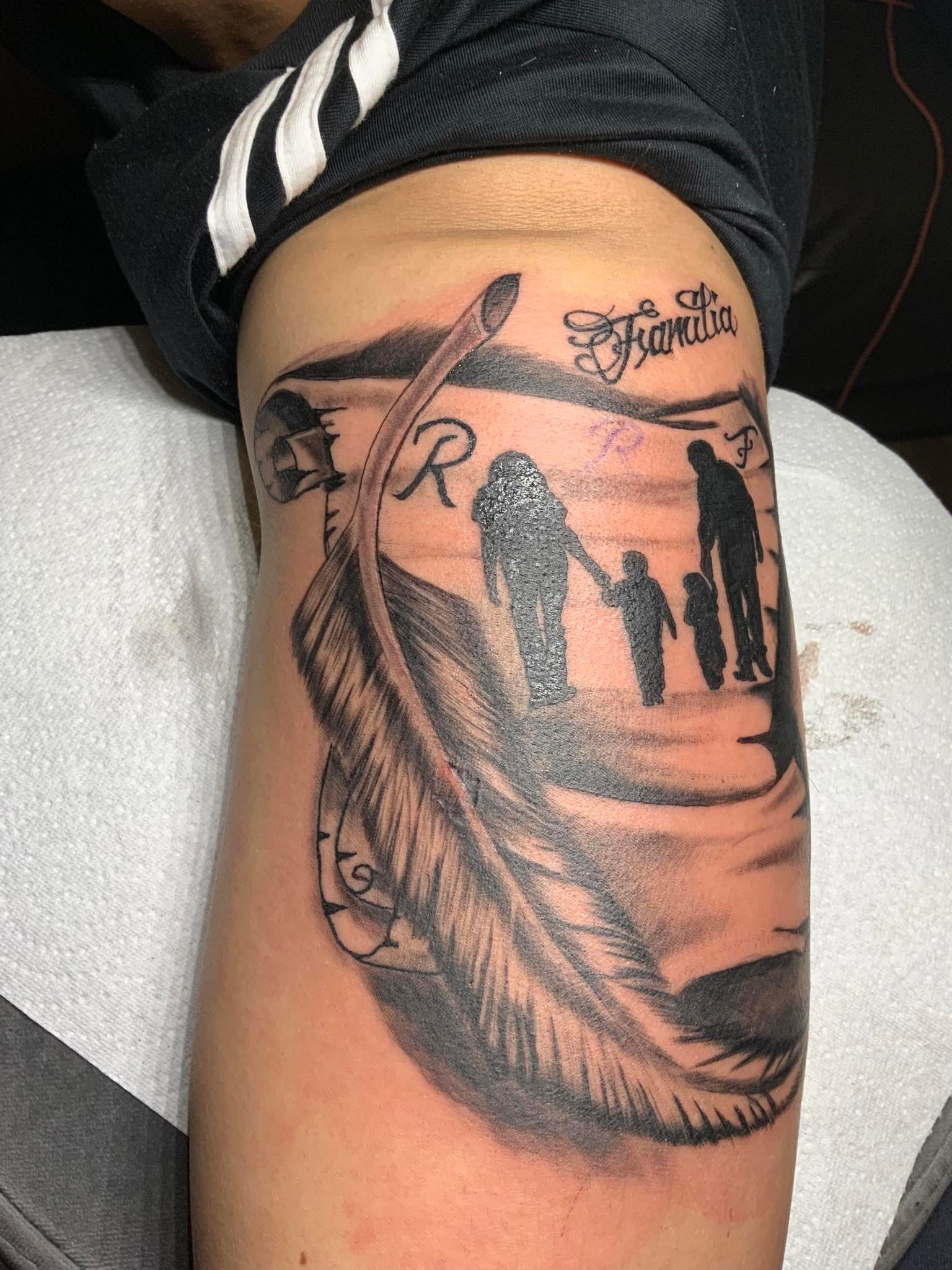 Tattoo of a feather next to a piece of paper that shows a happy family
